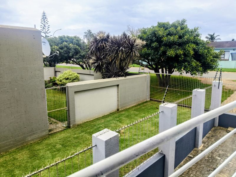 A view of the rear garden area featuring a lawn, boundary walls with electric fencing, and a paved section.