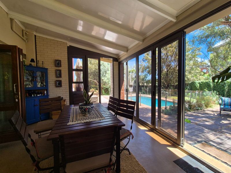 A bright, covered patio area featuring bi-fold glass doors that open onto a swimming pool and garden, providing a seamless indoor-outdoor living space.