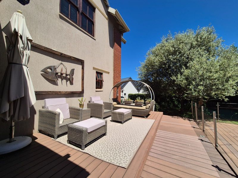 A well-maintained outdoor timber deck featuring a glass balustrade, providing a pleasant space for relaxation adjacent to the main house structure.