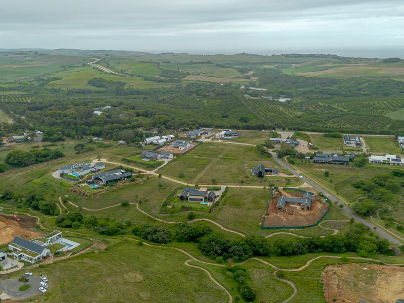 An aerial view of a residential estate development featuring established homes, vacant plots, and surrounding natural landscape.