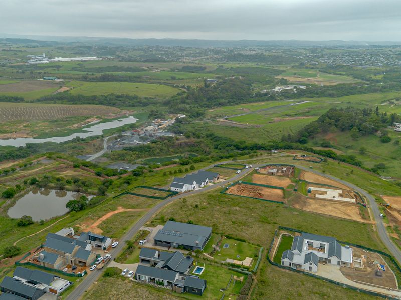 Aerial view of a developing residential estate featuring established homes, vacant plots, and surrounding natural landscape.