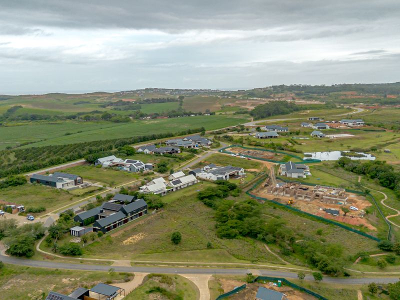 An aerial view of a residential estate development featuring modern homes, paved infrastructure, and surrounding green landscape under a cloudy sky.