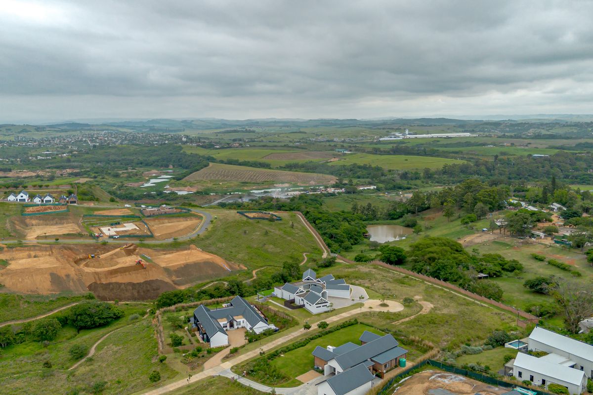 An aerial view of a residential estate development featuring modern homes, paved roads, and surrounding green landscape under a cloudy sky.