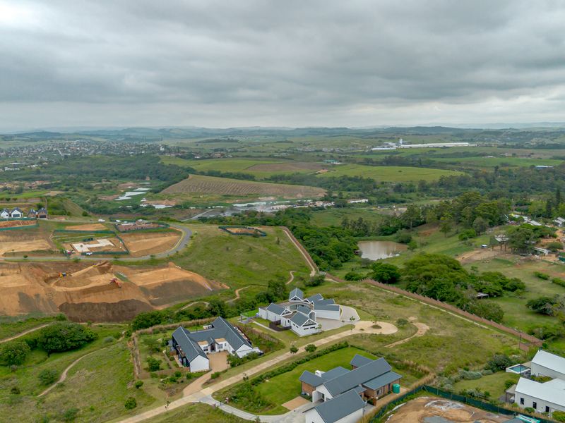 An aerial view of a residential estate development featuring modern homes, paved roads, and surrounding green landscape under a cloudy sky.