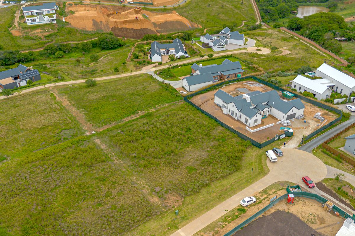 Aerial view of a vacant residential plot within a developed estate, featuring surrounding infrastructure and established neighboring homes.