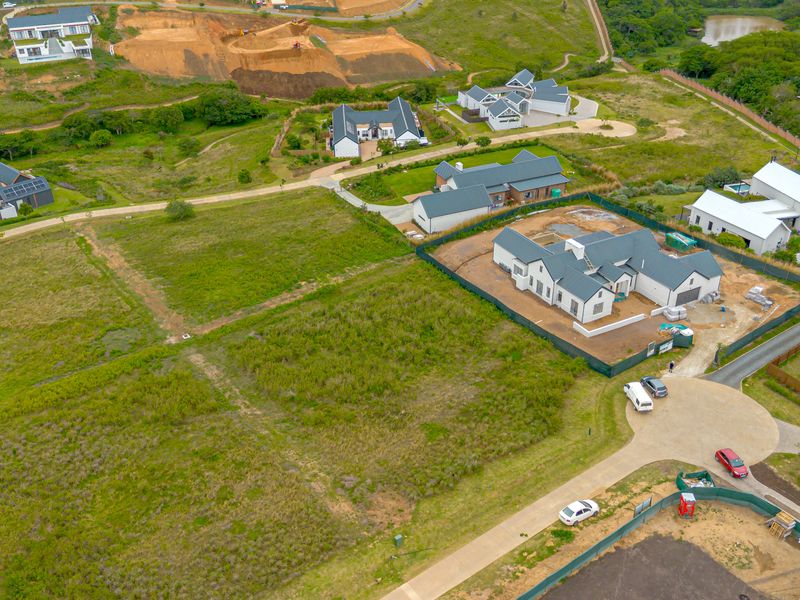 Aerial view of a vacant residential plot within a developed estate, featuring surrounding infrastructure and established neighboring homes.