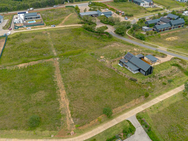 An aerial view of a vacant residential plot situated within a developed estate, featuring established access roads and surrounding modern homes.