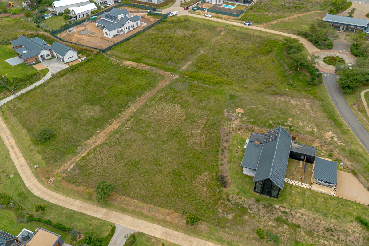An aerial view of a vacant residential plot situated within a developed estate, featuring established access roads and surrounding modern residential properties.