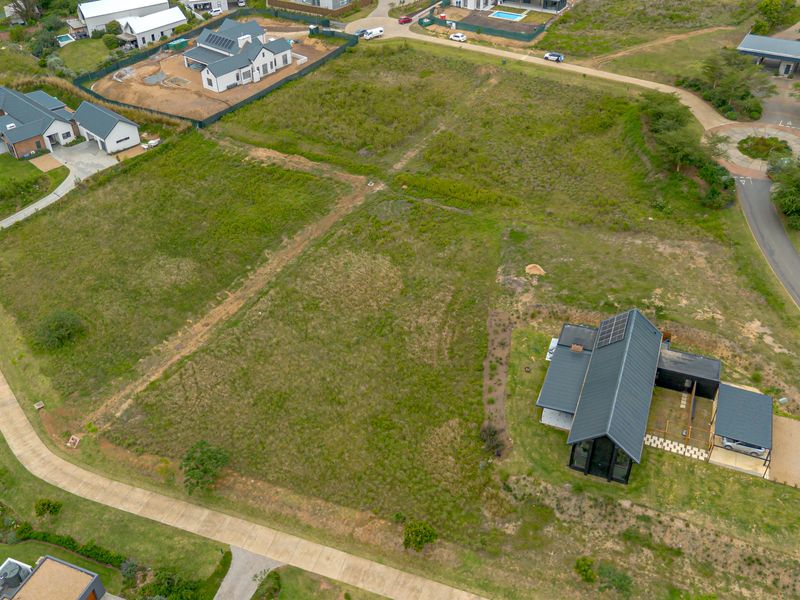 An aerial view of a vacant residential plot situated within a developed estate, featuring established access roads and surrounding modern residential properties.