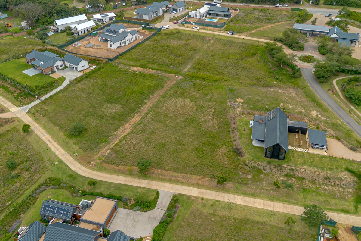 An aerial view of a vacant residential plot situated within a developed estate, featuring established access roads and surrounding modern homes.