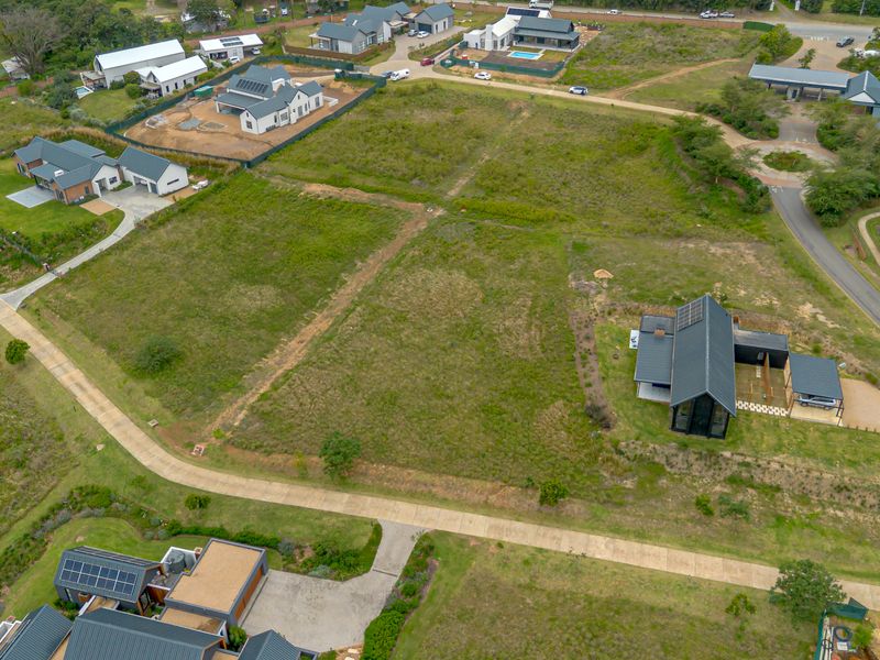 An aerial view of a vacant residential plot situated within a developed estate, featuring established access roads and surrounding modern homes.