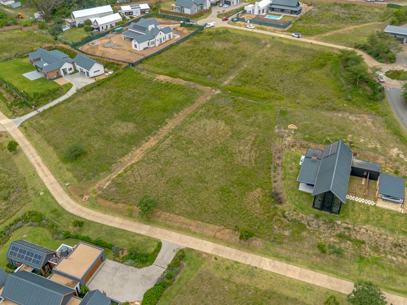 Aerial view of a vacant residential plot situated within a developed estate, featuring established access roads and neighboring modern homes.