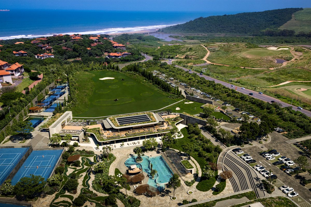 Aerial view of a coastal estate featuring a clubhouse, swimming pool, tennis courts, and golf course set within a landscaped environment.
