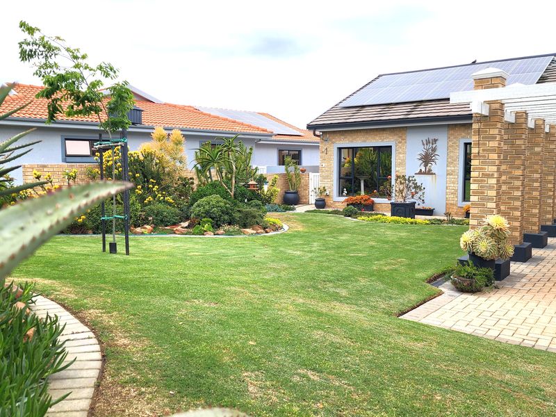A well-maintained rear garden featuring a paved patio area, pergola, and established landscaping, complemented by a brick-faced home with solar panels.