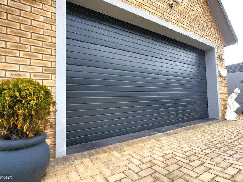 A modern sectional garage door set within a brick facade, featuring a paved driveway approach.