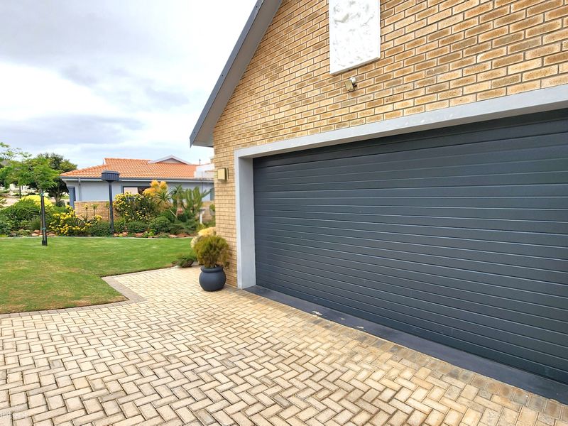A well-maintained front exterior featuring a modern dark grey sectional garage door, brick facade, and a neat paved driveway adjacent to a landscaped garden.