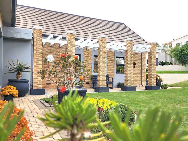 A well-maintained covered patio featuring brick pillars and a pergola, overlooking a landscaped garden area.