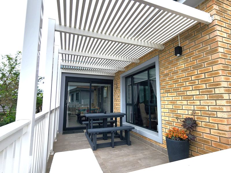 A well-maintained covered patio featuring a modern slatted pergola, brick exterior wall, tiled flooring, and direct access to the interior via sliding glass doors.