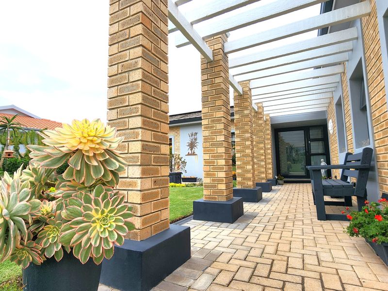 A well-maintained covered patio featuring brick columns, a timber pergola, and paved flooring, providing a seamless transition to the garden.