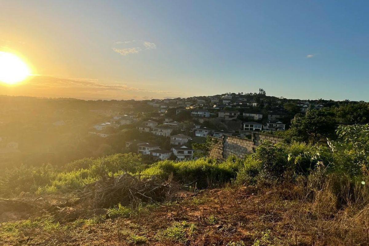 A scenic elevated view overlooking a residential neighborhood at sunset, featuring a vacant plot of land with a partial retaining wall.