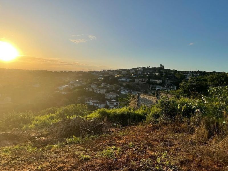 A scenic elevated view overlooking a residential neighborhood at sunset, featuring a vacant plot of land with a partial retaining wall.