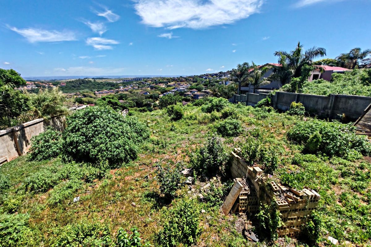 A sloped residential vacant land plot featuring a perimeter boundary wall and expansive views of the surrounding neighborhood.