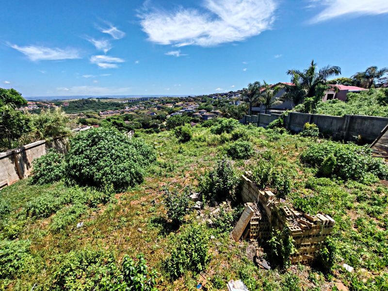 A sloped residential vacant land plot featuring a perimeter boundary wall and expansive views of the surrounding neighborhood.