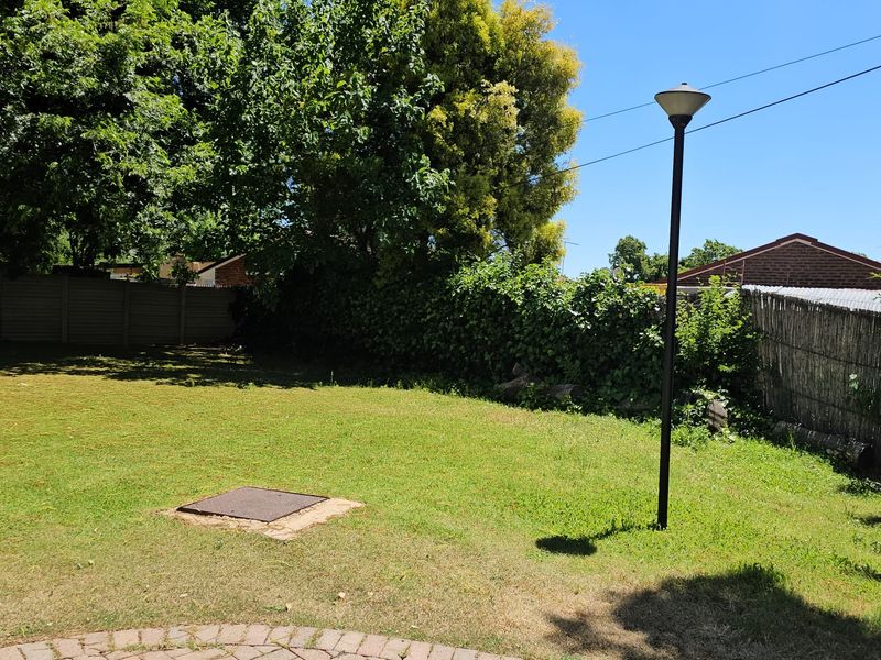 A spacious garden area featuring a paved patio, a central lawn, a boundary wall, and a fixed garden lamp post.