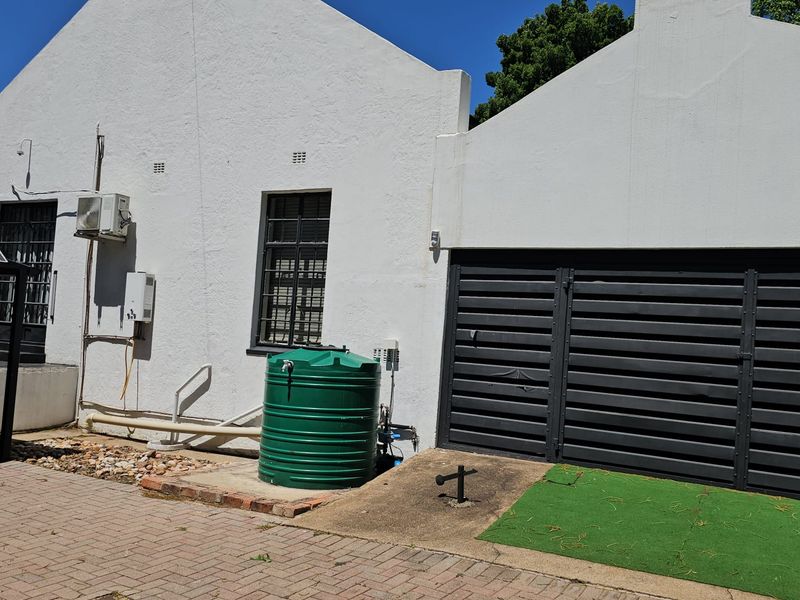 Rear exterior view of the guest house featuring a paved driveway, water storage tank, security lighting, and a gated entrance.
