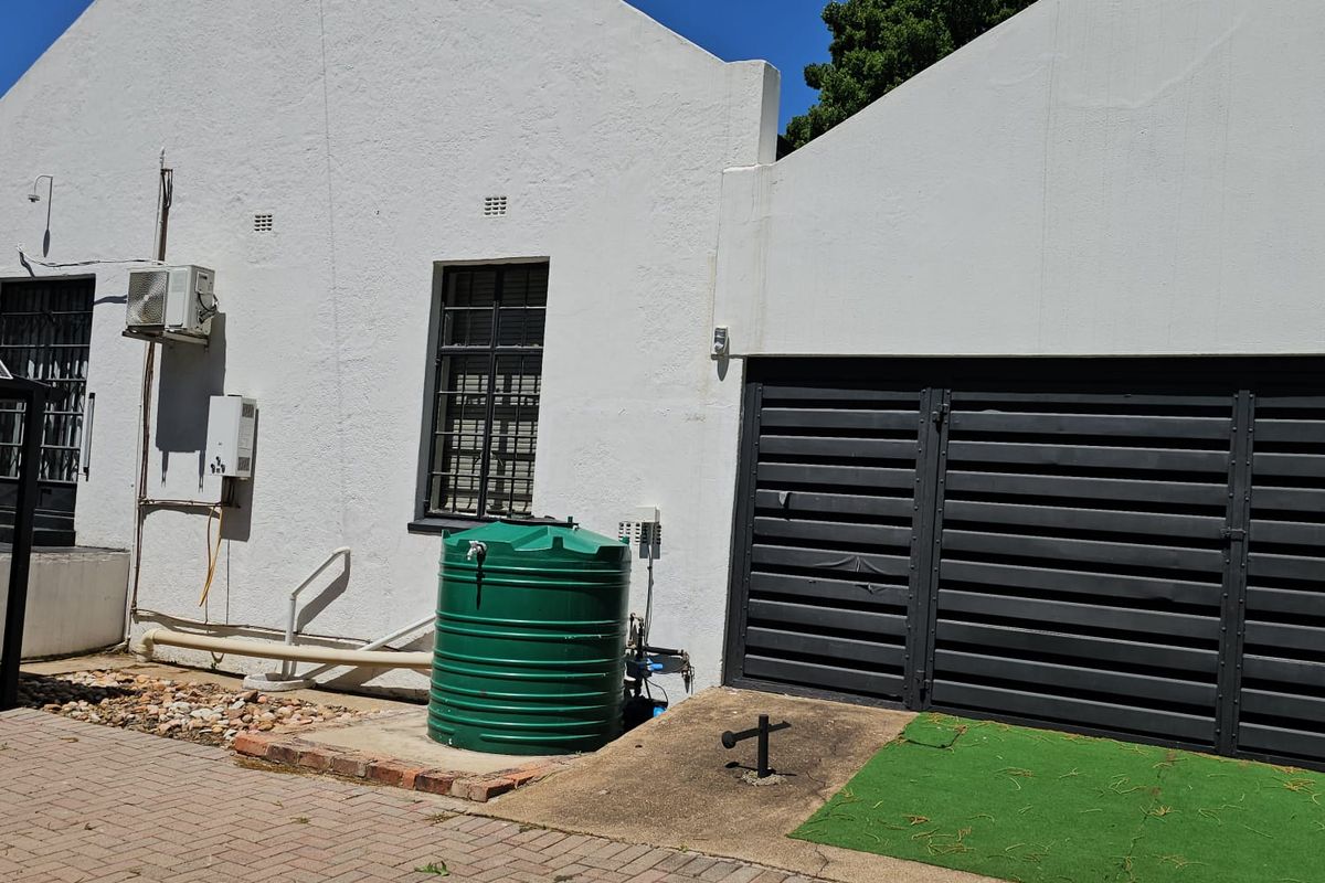 Rear exterior view of the guest house featuring a paved driveway, water storage tank, security lighting, and a gated entrance.