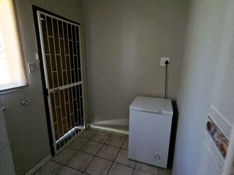 A functional scullery or utility area featuring tiled flooring and a secure metal gate leading to the exterior.