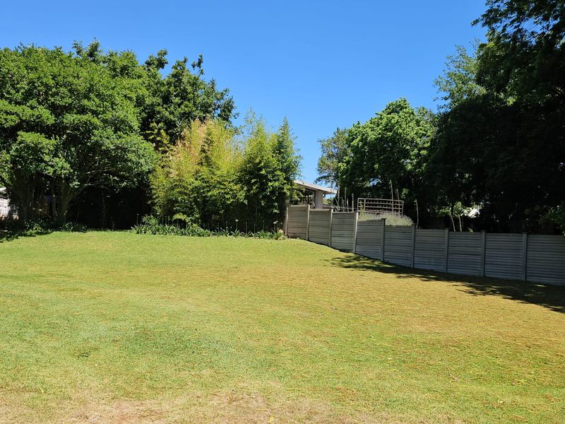 A spacious, well-maintained garden area featuring a large lawn, mature trees, and a secure precast concrete boundary wall.