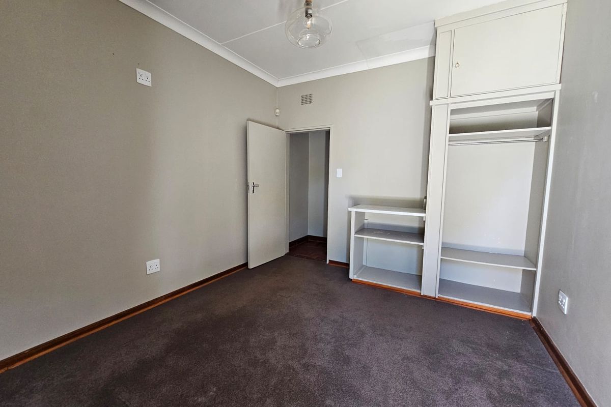 An empty bedroom featuring neutral walls, carpet flooring, and a built-in wardrobe with overhead storage.