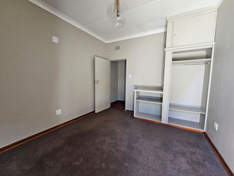 An empty bedroom featuring neutral walls, carpet flooring, and a built-in wardrobe with overhead storage.