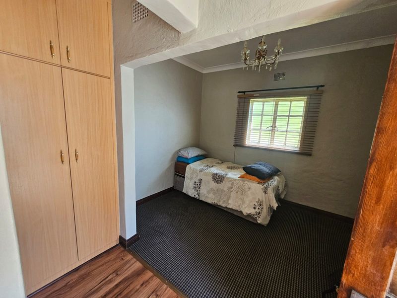 A bedroom featuring a built-in wardrobe, textured walls, and a window with blinds, offering a functional space with potential for cosmetic updates.
