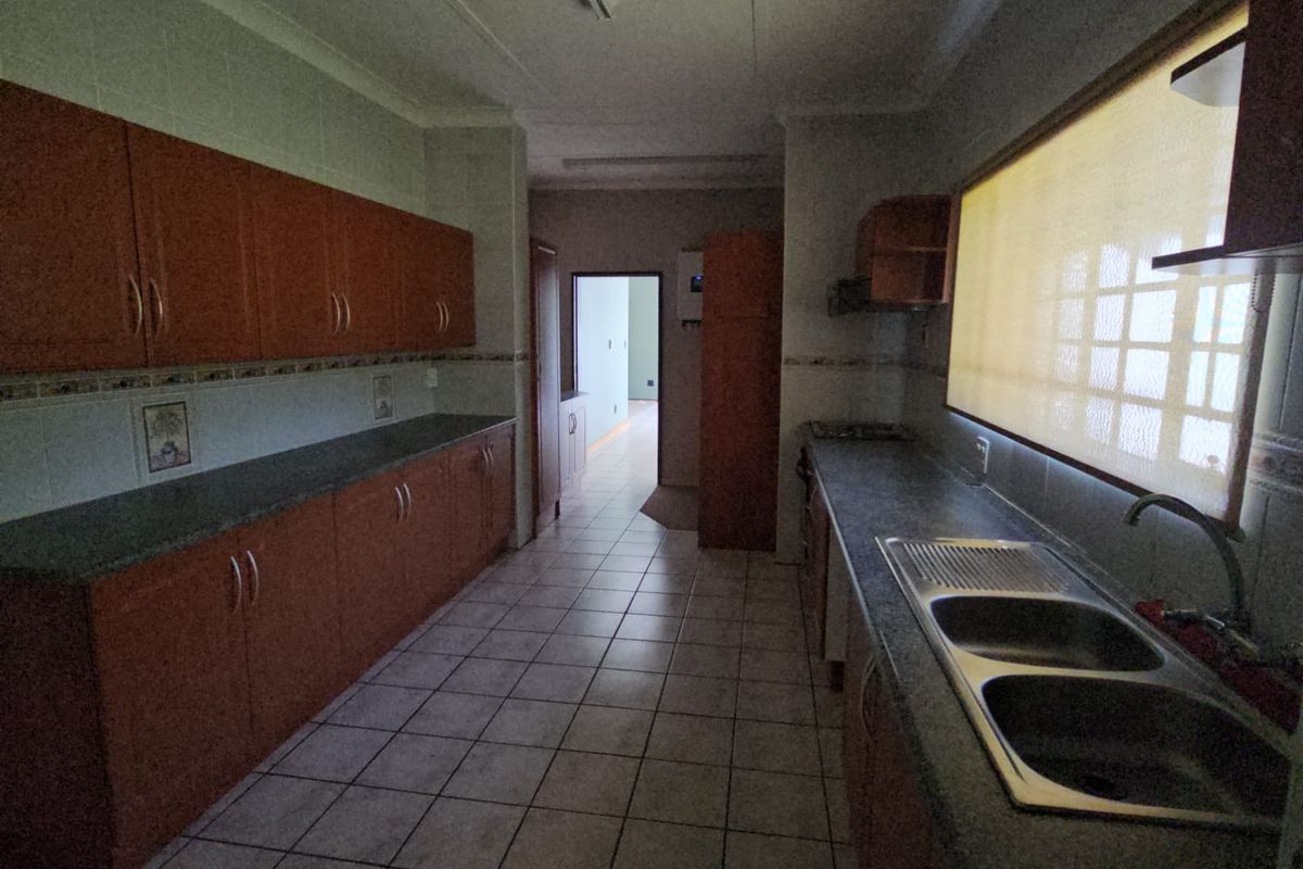 A functional kitchen featuring extensive wooden cabinetry, laminate countertops, a double stainless steel sink, and tiled flooring, offering a practical layout for food preparation.