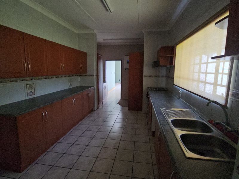 A functional kitchen featuring extensive wooden cabinetry, laminate countertops, a double stainless steel sink, and tiled flooring, offering a practical layout for food preparation.
