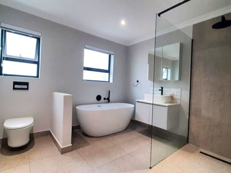 Modern bathroom featuring a sleek freestanding bathtub, walk-in shower with glass screen, wall-hung toilet, and contemporary vanity with matte black fixtures.