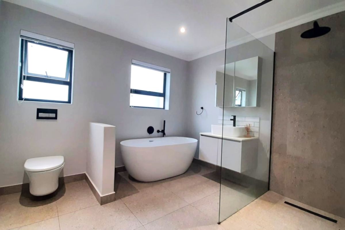 Modern bathroom featuring a sleek freestanding bathtub, walk-in shower with glass screen, wall-hung toilet, and contemporary vanity with matte black fixtures.