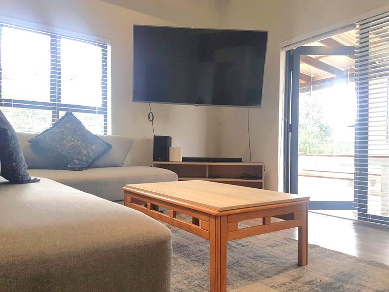 A bright living room featuring laminate flooring, large windows, and an aluminium sliding door providing direct access to the outdoor patio area.