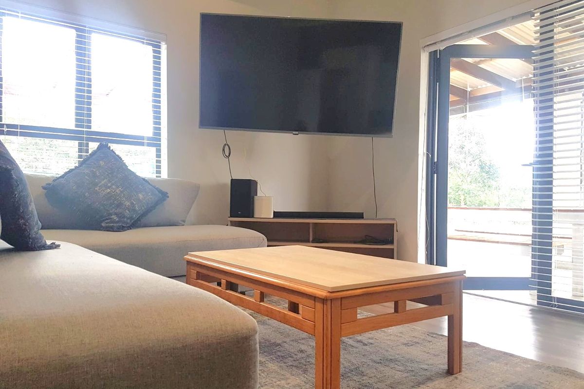 A bright living room featuring laminate flooring, large windows, and an aluminium sliding door providing direct access to the outdoor patio area.