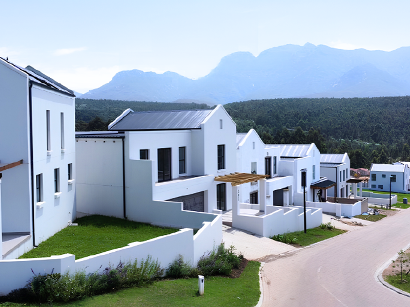 A row of modern white residential houses with timber pergolas and paved driveways, set against a scenic mountain backdrop.