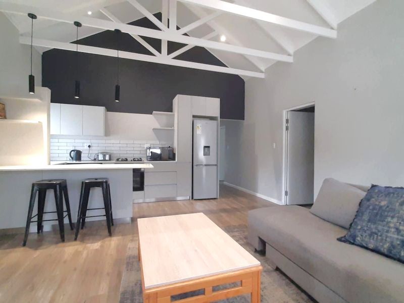 Modern open-plan living area featuring a vaulted ceiling with exposed trusses, sleek kitchen cabinetry, subway tile backsplash, and durable laminate flooring.
