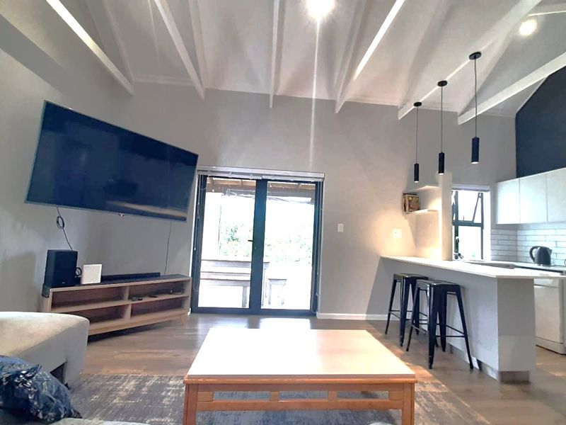 Spacious open-plan living area featuring a modern kitchen with island, vaulted ceilings with exposed beams, and direct access to the outdoor patio.