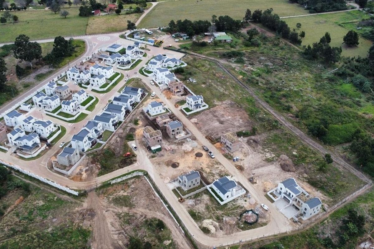 Aerial view of a residential housing development showing completed homes, ongoing construction, paved internal roads, and perimeter fencing.