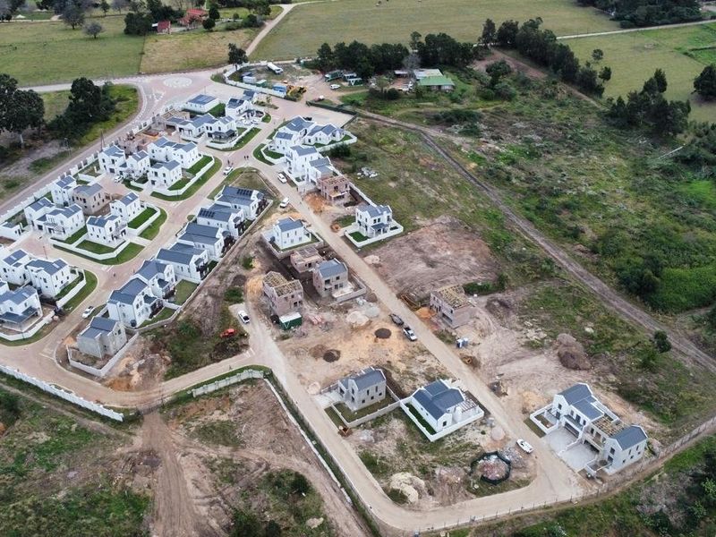 Aerial view of a residential housing development showing completed homes, ongoing construction, paved internal roads, and perimeter fencing.
