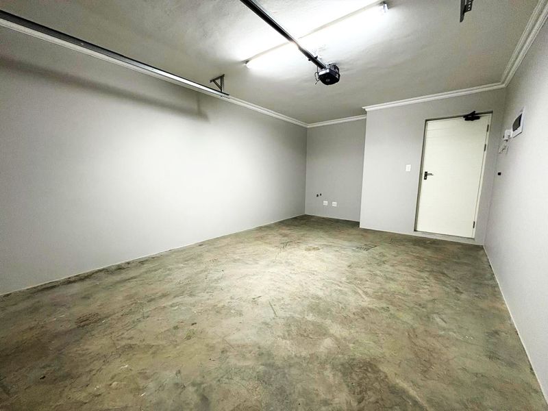 A clean, empty garage space featuring concrete flooring, a garage door motor, and functional overhead lighting.