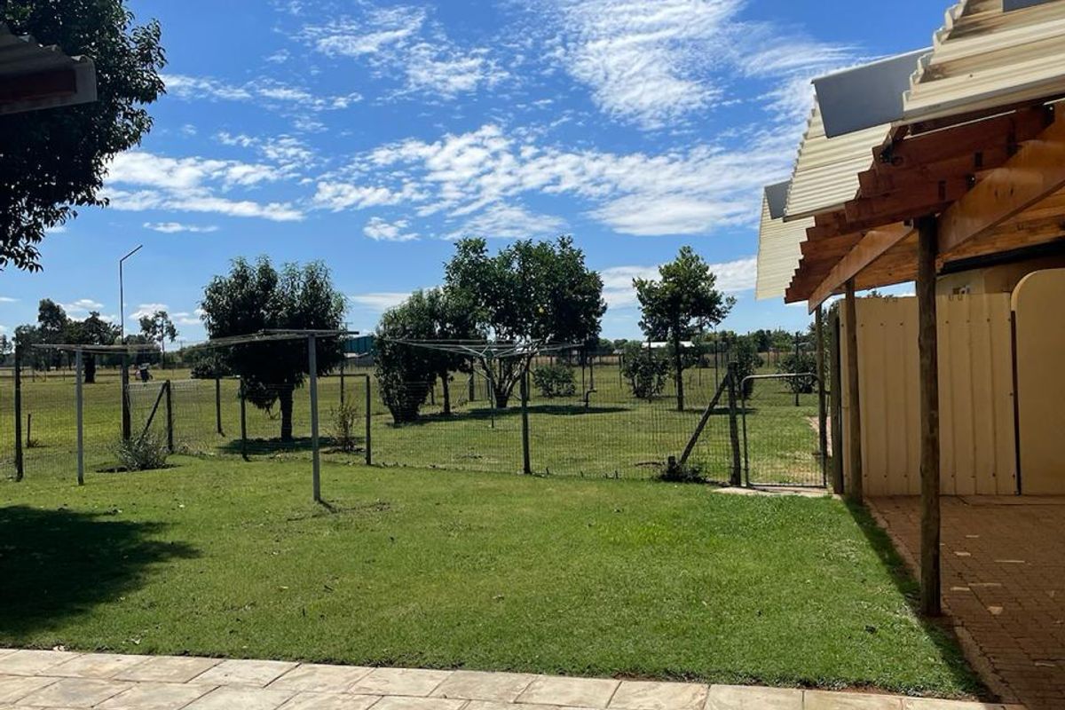A spacious rear garden featuring a paved walkway, covered patio area, and established lawn enclosed by wire fencing.