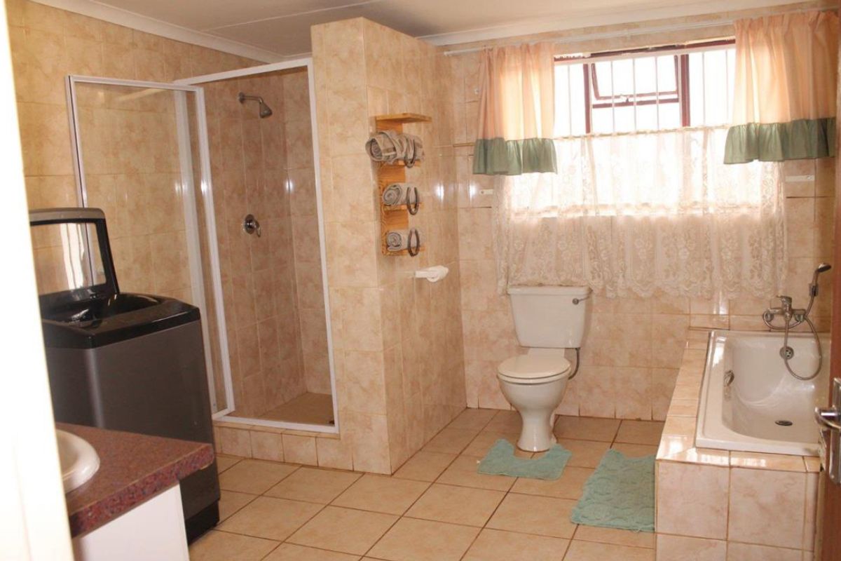 A functional bathroom featuring a shower enclosure, built-in bathtub, toilet, and tiled finishes throughout, offering a practical layout with natural light.