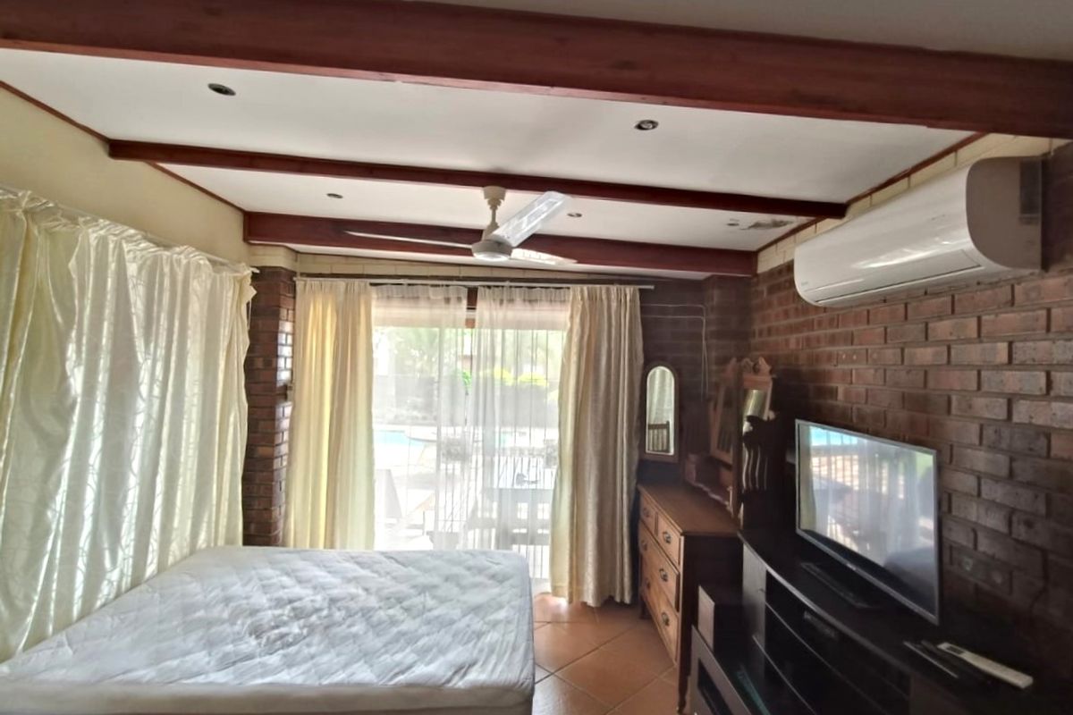 Bedroom featuring exposed brick walls, timber ceiling beams, tiled flooring, and a split-system air conditioner with direct access to the outdoor area.